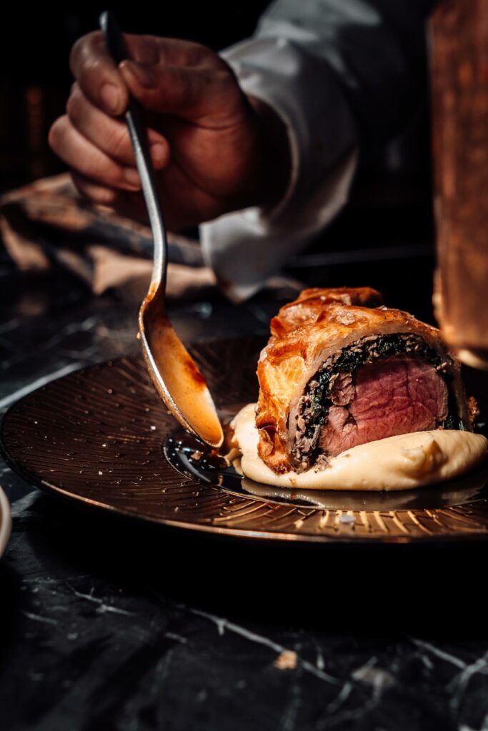 A large cut of beef wellington getting plated by the chef